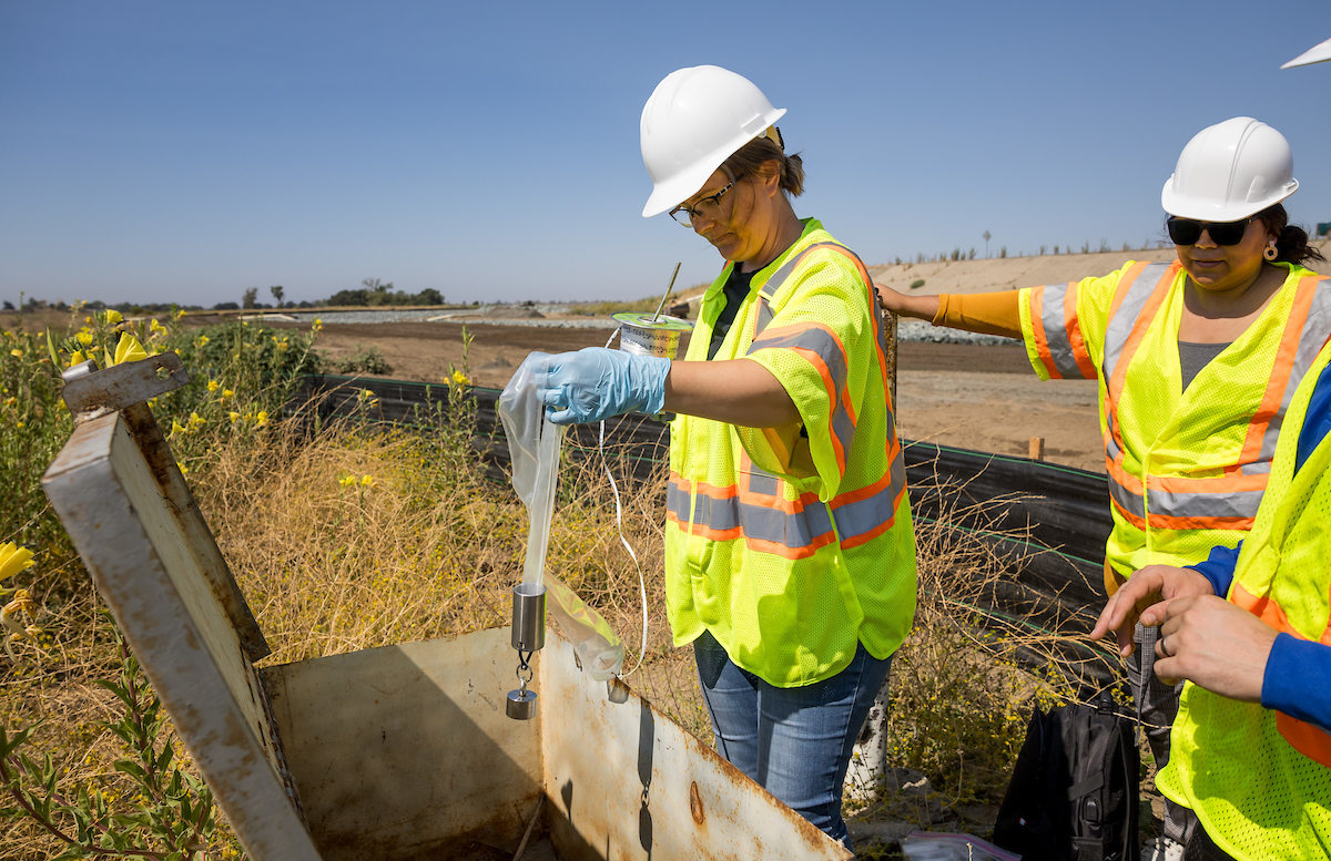 Engineering Geologists Sonja Dreuth (center) and Nicholas Vadpey from the California Department of Water Resources North Central Region Office, in the Division of Regional Assistance, collect groundwater quality samples using a no-purge bailer water sampling device at a monitoring well at the Sacramento Bypass in Yolo County. Student Assistant Guadalupe Ferreyra (right), who also monitors the well, lends support. Photo taken August 30, 2024.