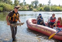 DWR biologist displaying a salmon carcass to three individuals on a raft at Feather River.