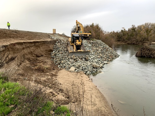 Bulldozer pushing rock riprap into damaged section of a levee